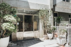 A building entrance with a glass door, potted plants, and a white fence.