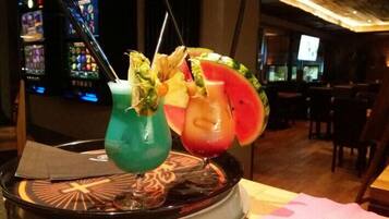 Two colorful cocktails with fruit garnishes on a bar counter in a dimly lit bar area.