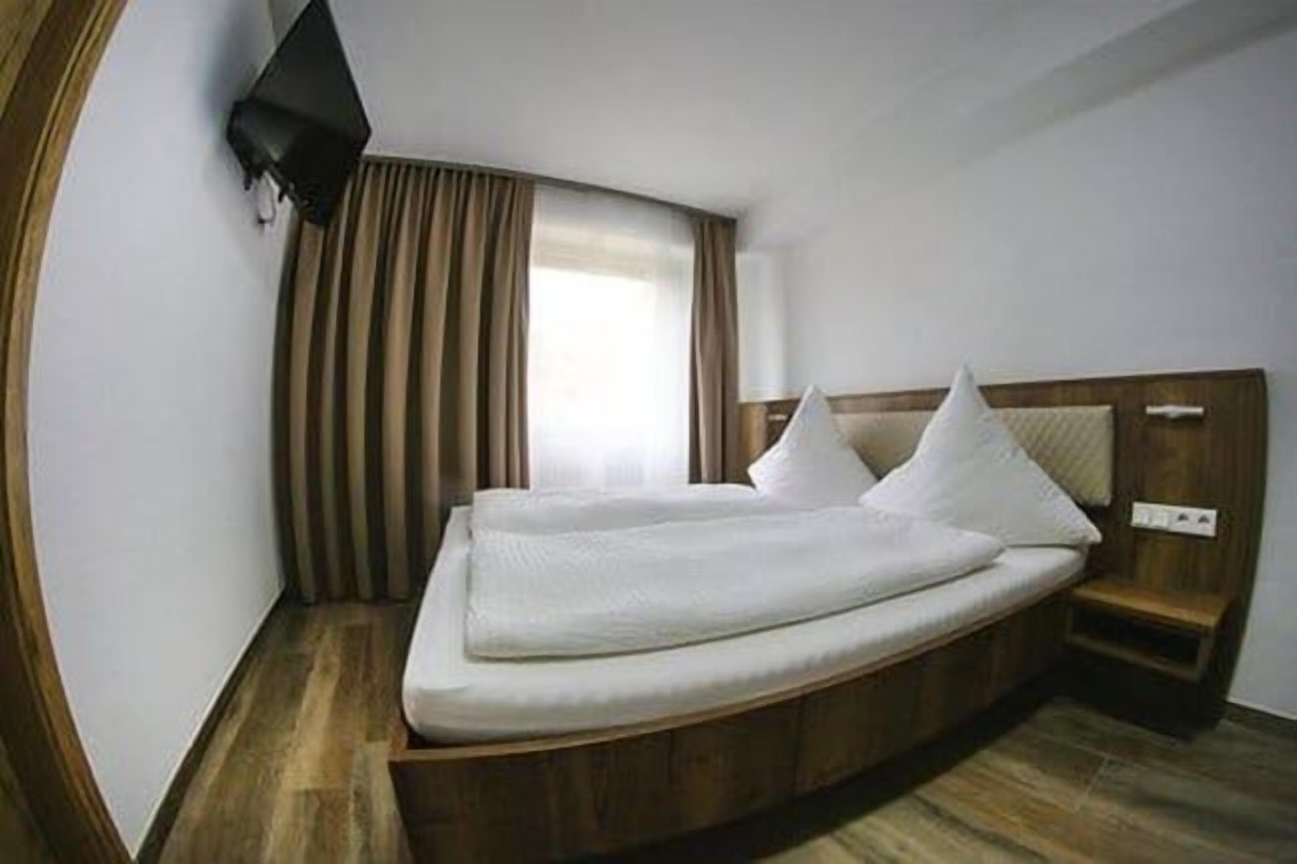 Una habitación de hotel moderna con una cama de madera, un televisor de pantalla plana y una ventana con cortinas.