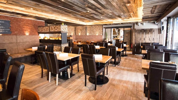A restaurant with wooden ceiling beams, stone walls, and a brick accent wall. Tables and chairs are arranged for dining. - LOOK Hotel & Rooms (Crailsheim)
