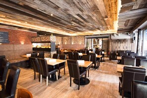 Ein Restaurant mit Holzbalkendecke, Steinwänden und einer Wand aus Ziegelsteinen. Tische und Stühle sind zum Essen bereitgestellt.