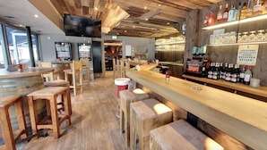 A bar area with wooden stools, a bar counter, and shelves with bottles and glasses. - LOOK Hotel & Rooms (Crailsheim)