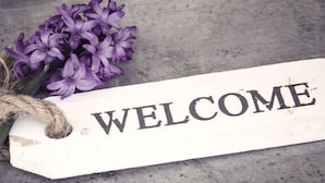 A wooden sign with the word "WELCOME" on it, placed on a concrete surface with a bunch of purple flowers beside it. - LOOK Hotel & Rooms (Crailsheim)