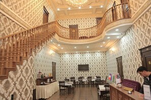 Un vestíbulo de hotel con una escalera monumental, una recepción y un área de estar con mesas y sillas.