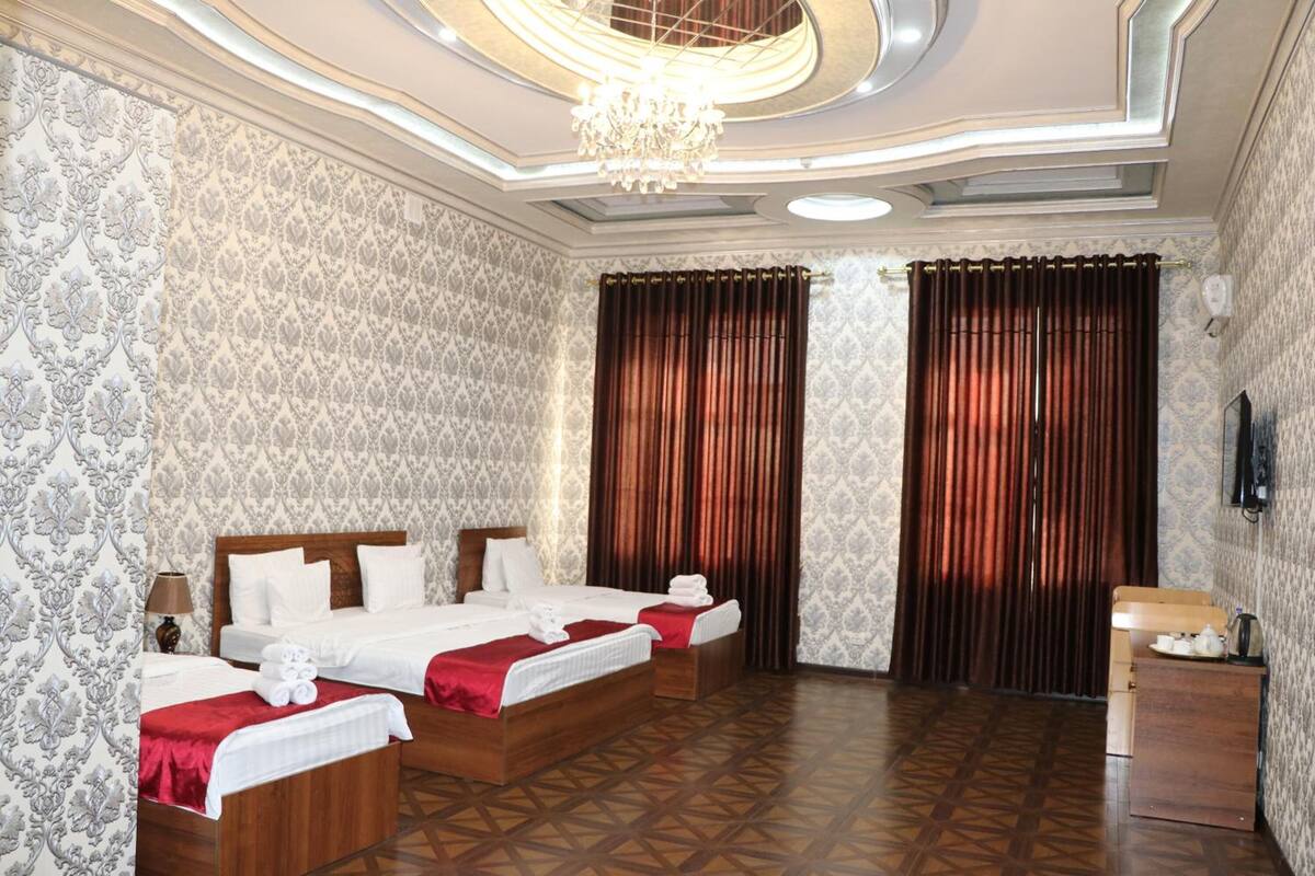 Ein Hotelzimmer mit zwei Betten, einem Holzkopfstück, einer Chandelüster und Wandtapete mit Muster.
