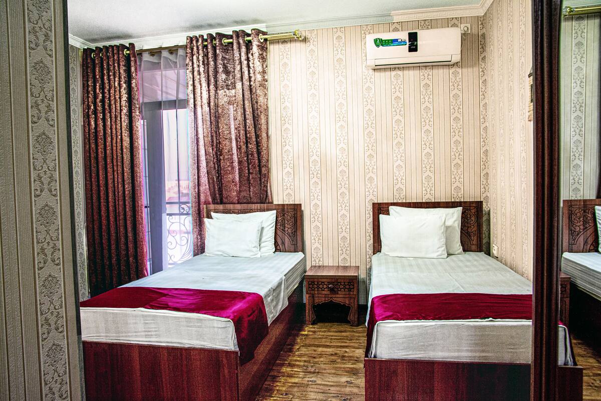 Ein Hotelzimmer mit zwei Betten, Holzboden, einem kleinen Nachttisch und einer Wandklimaanlage.