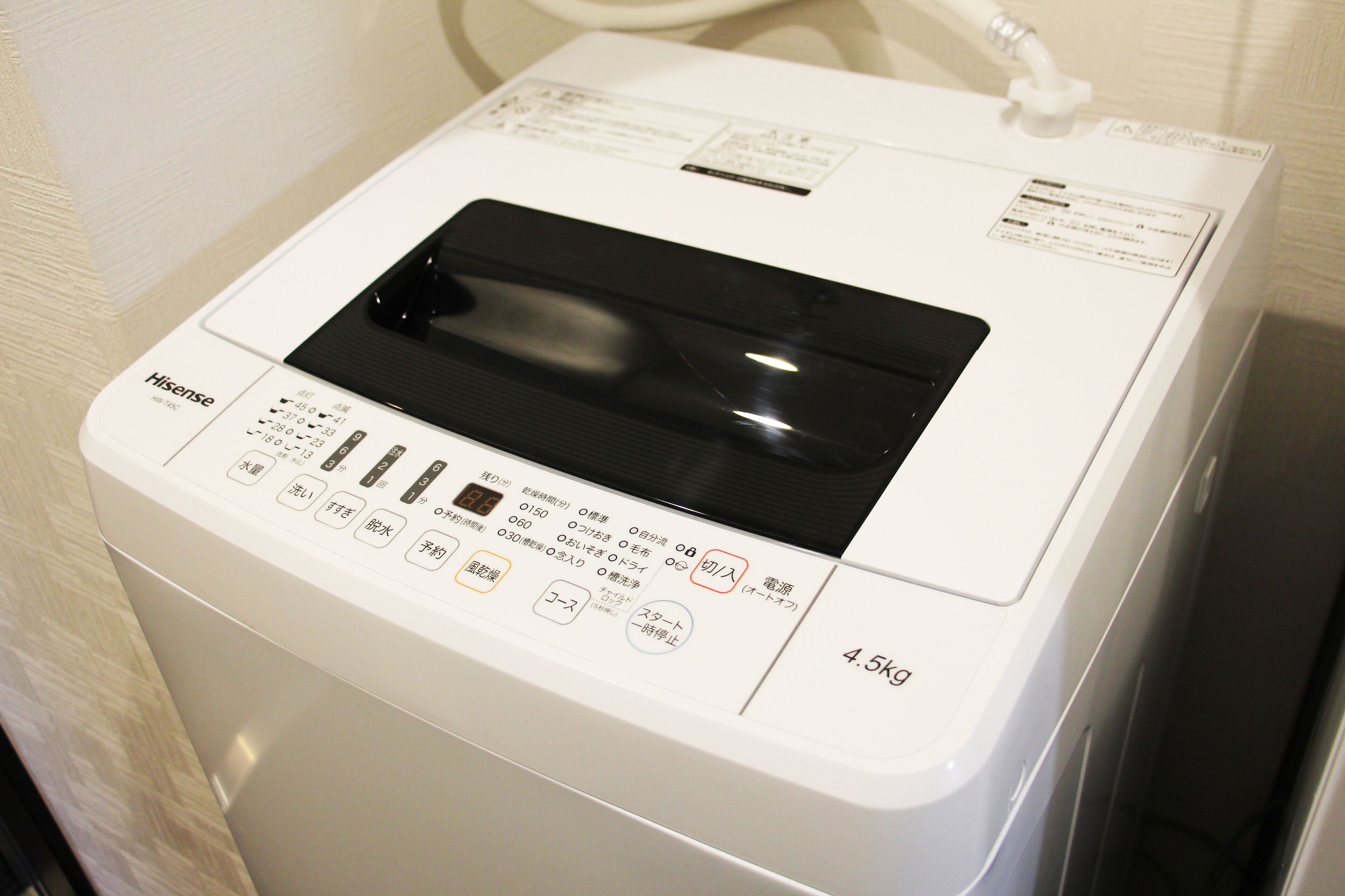 Una lavadora Hisense blanca con panel de control, etiqueta de capacidad de 4,5 kg y manguera de entrada de agua.