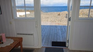 Une pièce avec un plancher en bois, une table recouverte d’une nappe en dentelle et une vue sur la plage, visible à travers une porte.