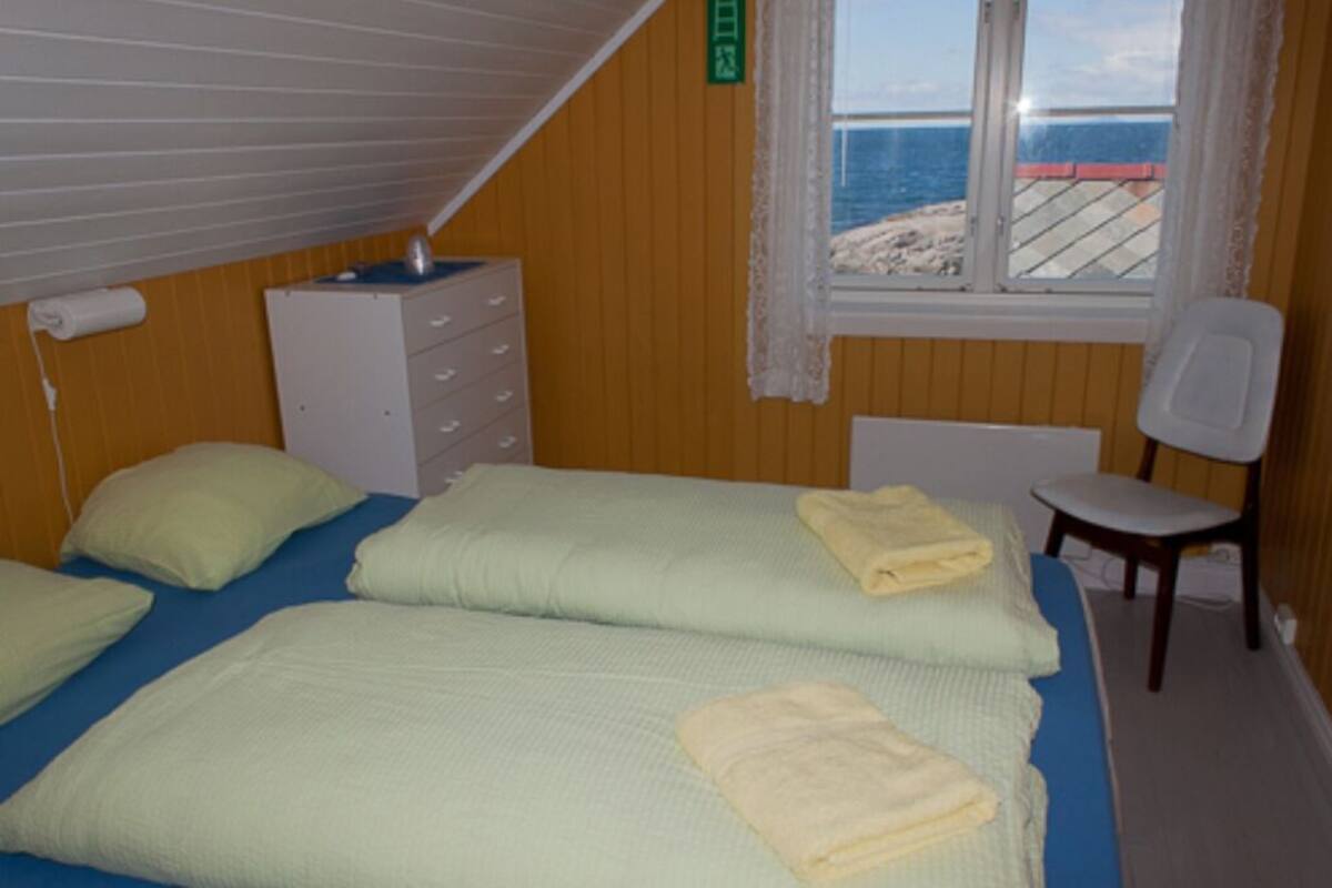 A room with two beds, a chair, a dresser, and a window with a view of the beach.