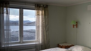 Une chambre avec deux lits, une fenêtre avec des rideaux, un radiateur et une table de chevet en bois avec une lampe.