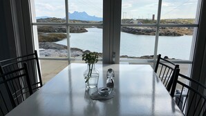 Une table avec un vase et une bouteille, donnant sur un paysage rocheux et une étendue d’eau.
