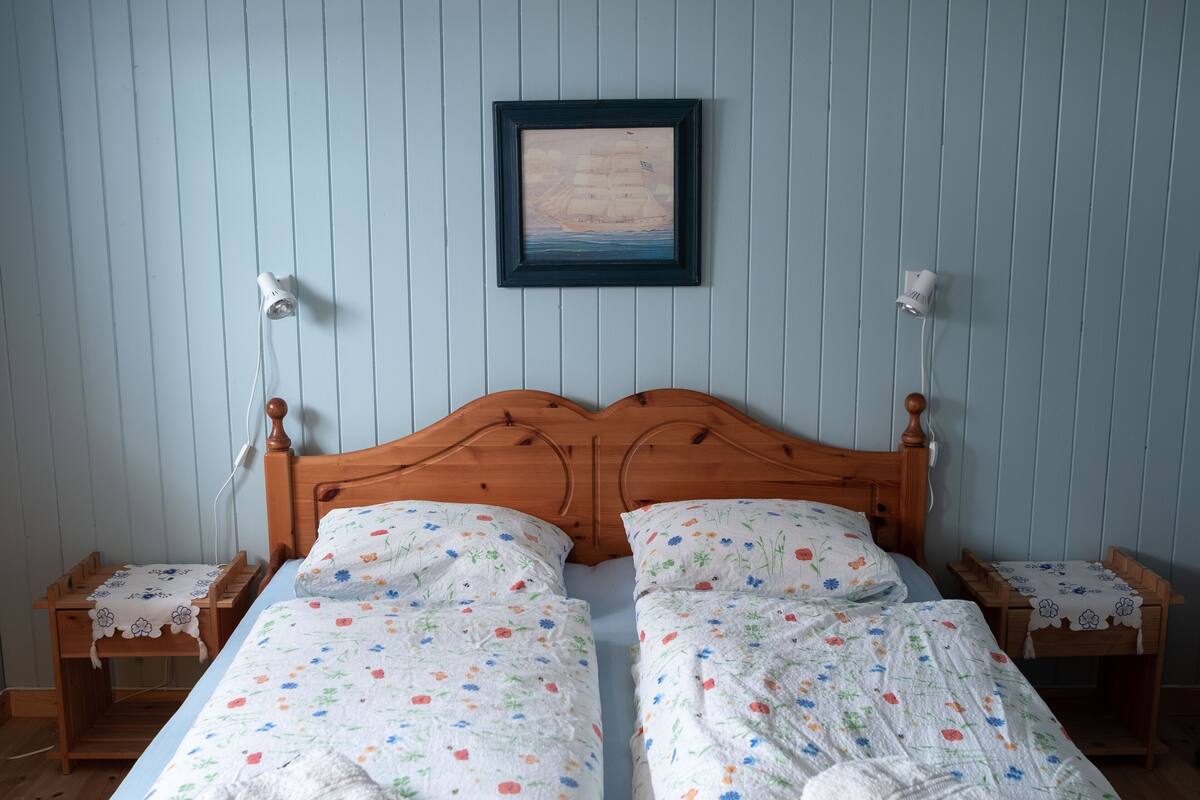 A double bed with floral bedding, a wooden headboard, bedside tables with lamps, and a framed picture on the wall.