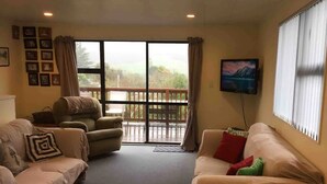 A living room with two sofas, a television, and a view of a balcony.