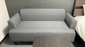 Harmaa sohva hotellihuoneessa, ja huoneessa on myös puinen sivupöytä sekä kuviollinen seinä.