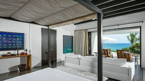 A modern hotel room with a large bed, a desk with a computer, a view of the ocean, and a balcony with outdoor furniture. - Casa Oliver (San José del Cabo)