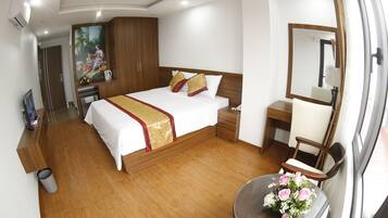 A hotel room with a bed, bedside table, chair, and a small table with flowers.