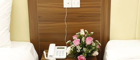 A hotel room with a wooden headboard, a bedside phone, and a bouquet of pink roses.