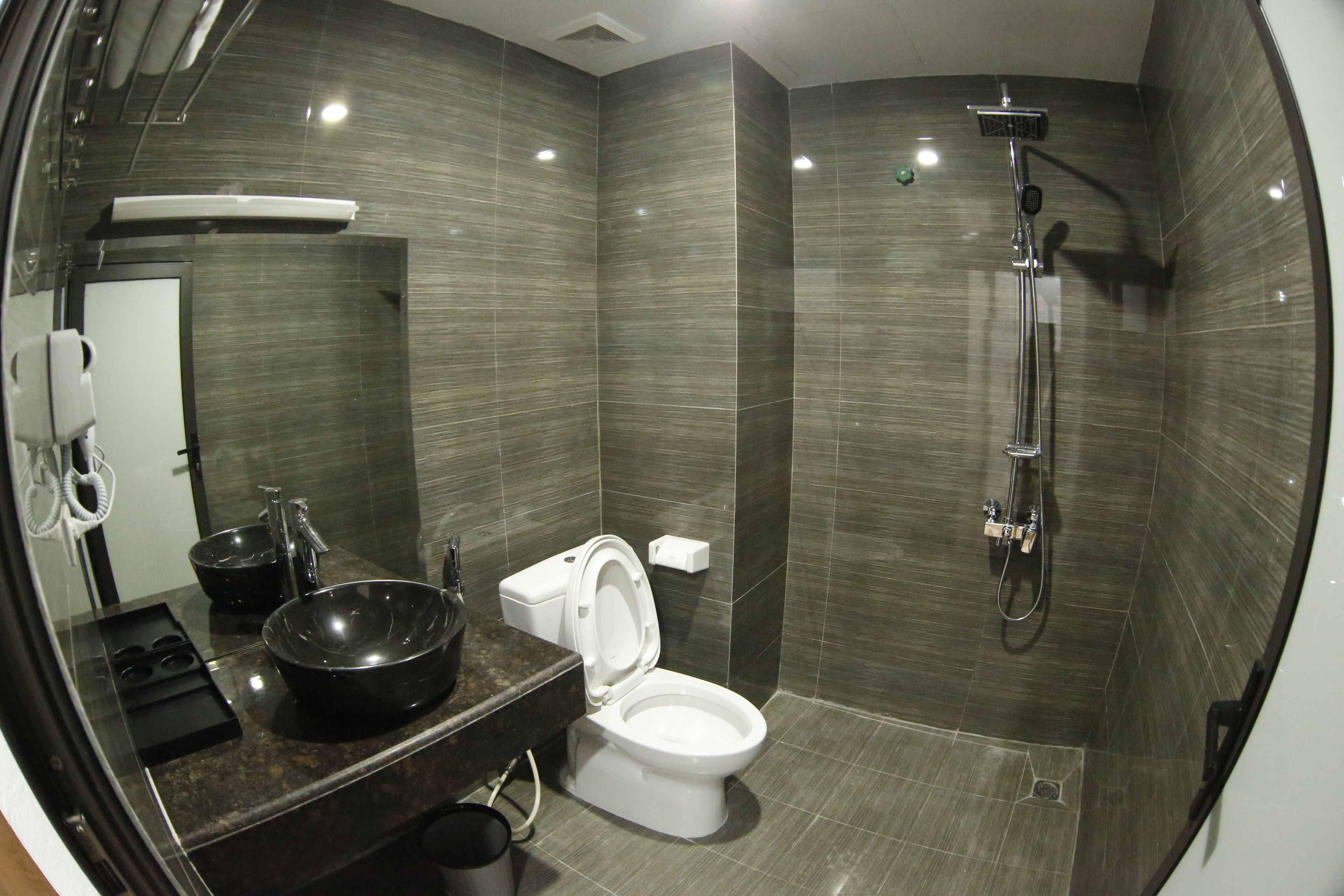 Un bagno moderno con uno specchio grande, un lavandino nero, un WC e una doccia.