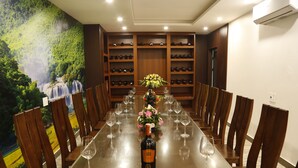 Une longue table à manger, des chaises, une bouteille de vin et des verres à vin.