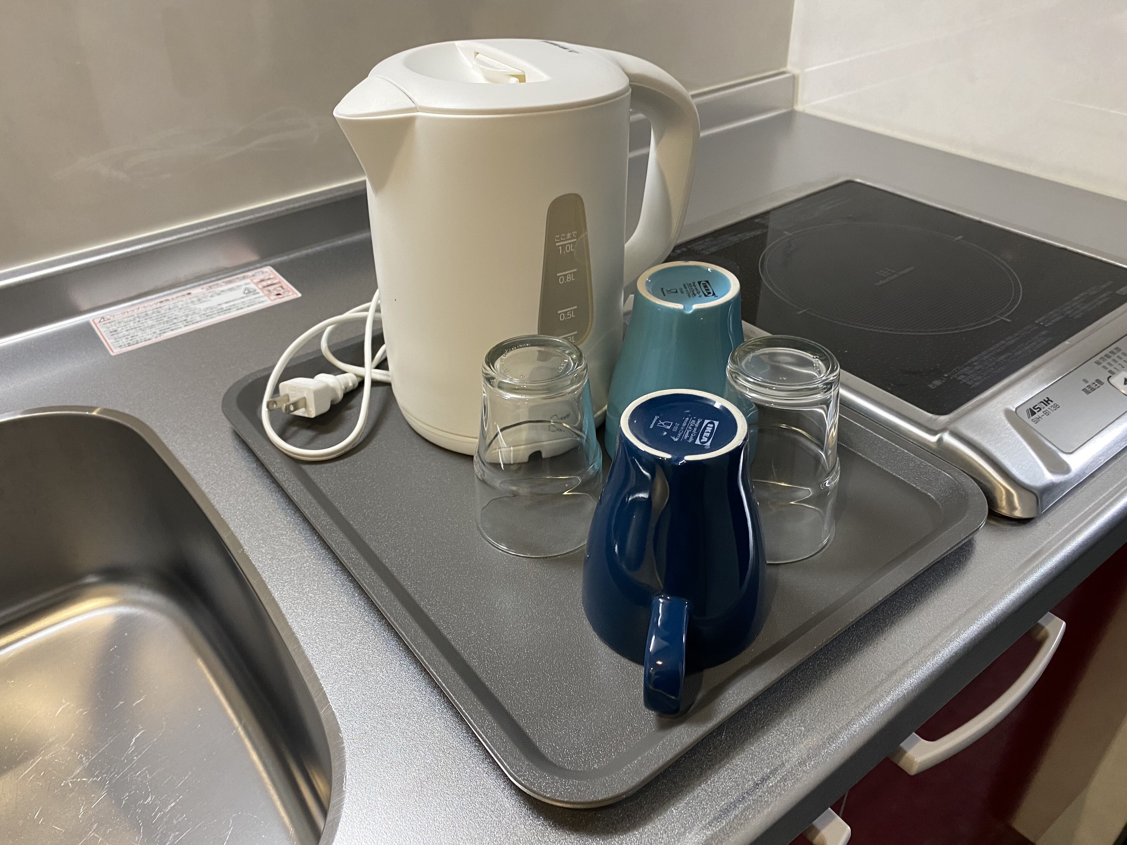 Un comptoir de cuisine avec une bouilloire électrique blanche, une tasse bleue et deux verres transparents.