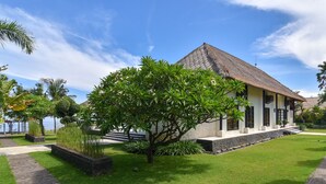 A two-story building with a thatched roof, surrounded by well-maintained grass and tropical plants. - Luxury Beach Front Villa with large garden, private pool, staff and free Wi-fi (Singaraja)