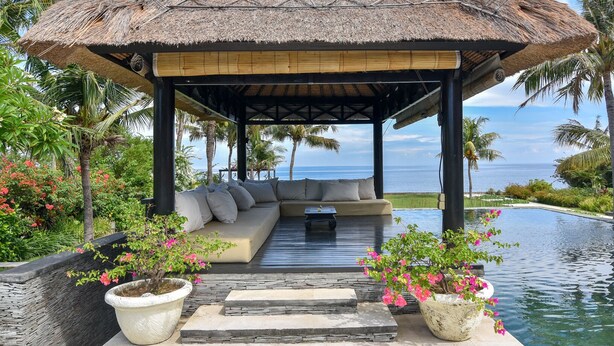 A covered outdoor seating area with a thatched roof, overlooking a pool and the ocean. - Luxury Beach Front Villa with large garden, private pool, staff and free Wi-fi (Singaraja)