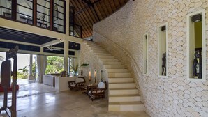 A spacious interior with a curved staircase, a high ceiling, and a stone wall. - Luxury Beach Front Villa with large garden, private pool, staff and free Wi-fi (Singaraja)