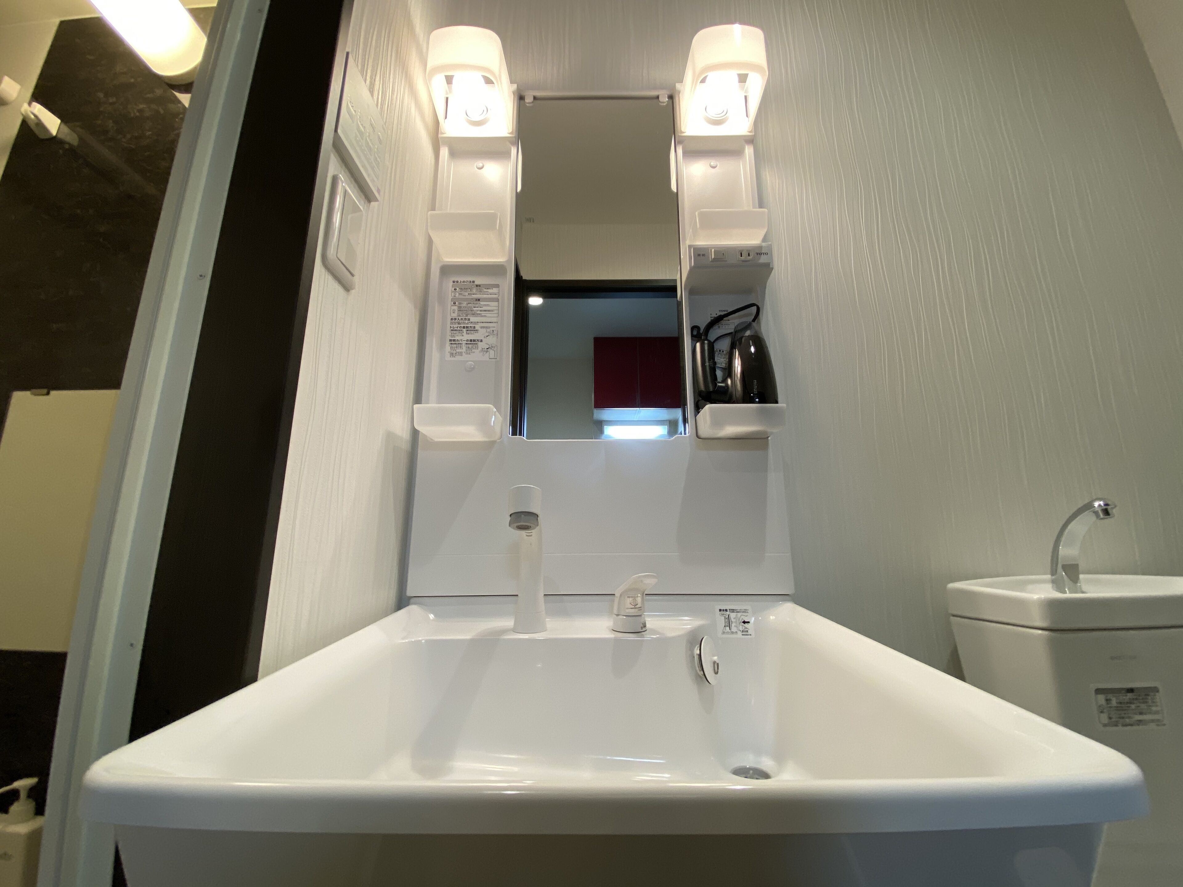 Un baño con un lavamanos blanco, dos espejos iluminados y un inodoro blanco.