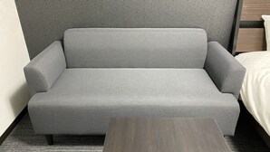 Ein graues Sofa in einem Hotelzimmer mit einem Holznachttisch und einer Wand mit Muster.