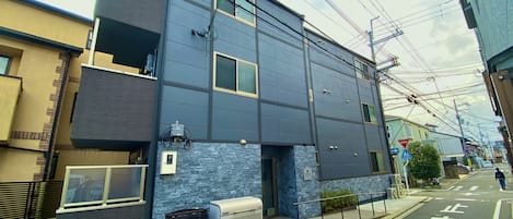 A modern building with a flat facade, multiple windows, and a visible air conditioning unit on the ground floor.