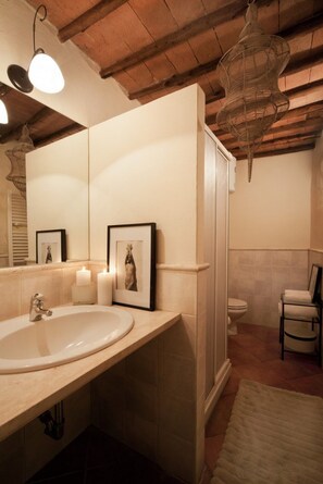 A bathroom with a large sink, two framed pictures, a white toilet, and a chair.