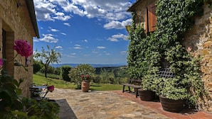 A stone patio with a bench, potted plants, and a view of a rural landscape. - La Grotta Della Rocca (Castellina in Chianti)
