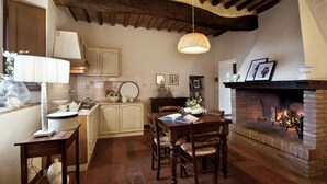 A cozy kitchen with a wooden ceiling, a dining table with chairs, a fireplace, and a hanging light fixture. - La Grotta Della Rocca (Castellina in Chianti)