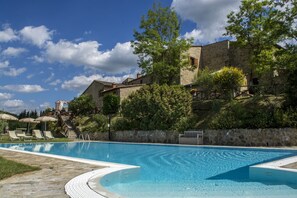 A swimming pool with lounge chairs and a stone building in the background.