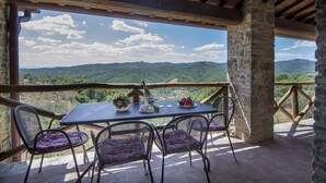 An outdoor dining area with a table and chairs, a view of green hills, and a stone pillar. - Typical, Charming With Chianti View (Bucine)