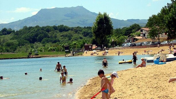 A beach with people swimming and relaxing, a mountain in the background, and houses along the shore. - Au Calme Wooden cottages 2 to 3 persons a couple and 1 small child (La Bastide-Clairence)