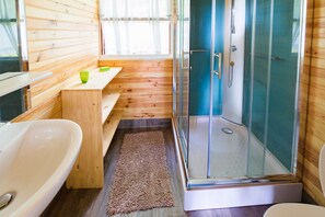 Een kleine badkamer met een houten inrichting, een douche met glazen wanden en een witte badkuip.