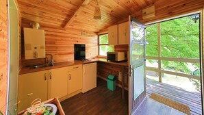 A wooden cabin with a kitchen, a sink, a stove, and a window overlooking greenery. - Au Calme Wooden cottages 2 to 3 persons a couple and 1 small child (La Bastide-Clairence)