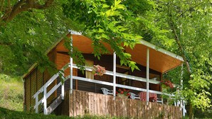 A wooden cabin with a balcony, surrounded by lush greenery. - Au Calme Wooden cottages 2 to 3 persons a couple and 1 small child (La Bastide-Clairence)