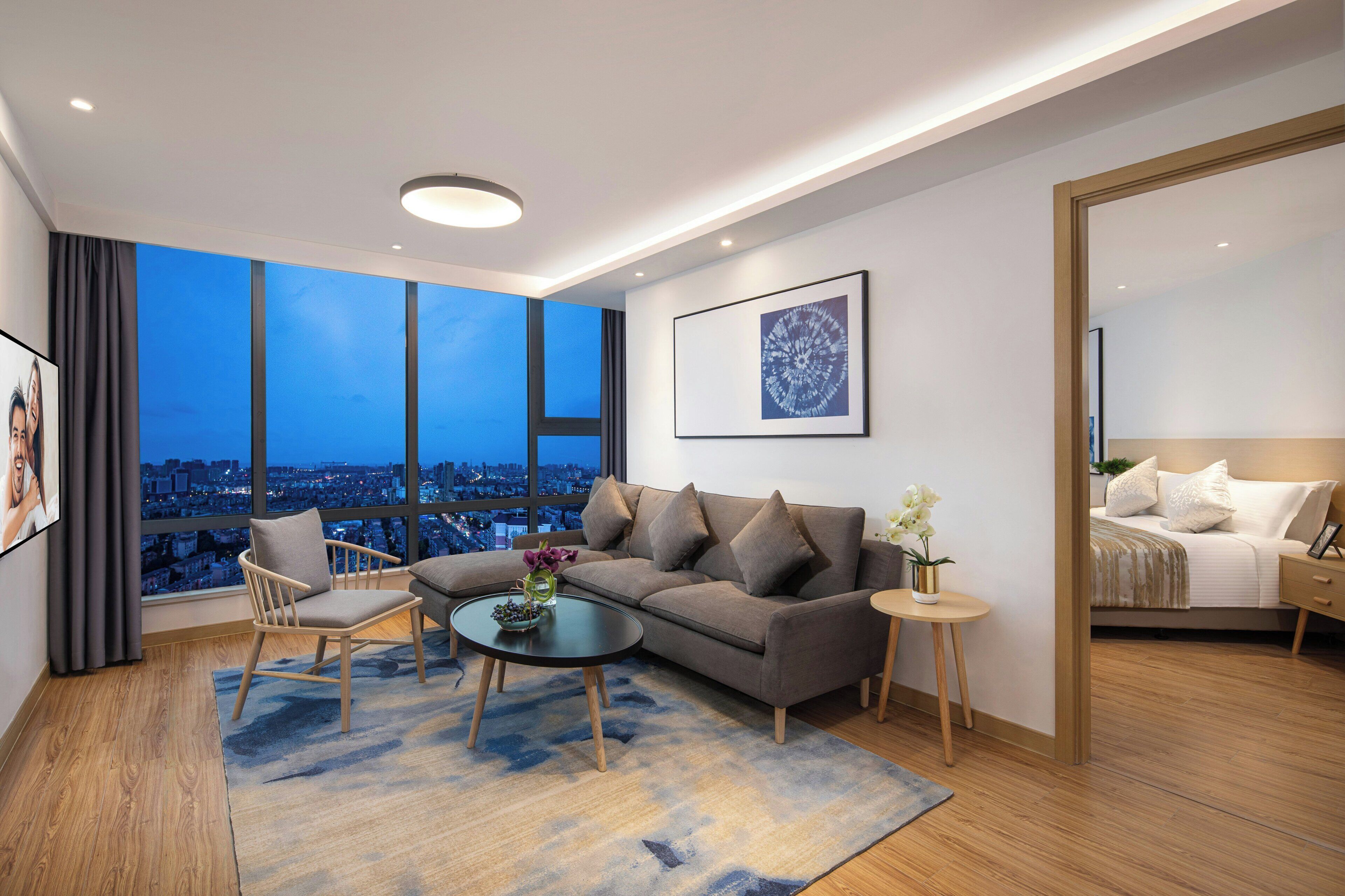 Un salon moderne avec un canapé, un fauteuil, une table basse et une vue sur le paysage urbain, visible à travers de grandes fenêtres.