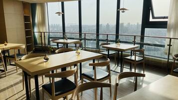 A modern restaurant with high tables and chairs, large windows offering a city view, and pendant lighting.