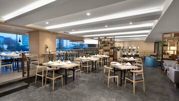 A modern restaurant with a spacious layout, featuring multiple dining tables and chairs, a bar area, and a view of the cityscape through large windows.