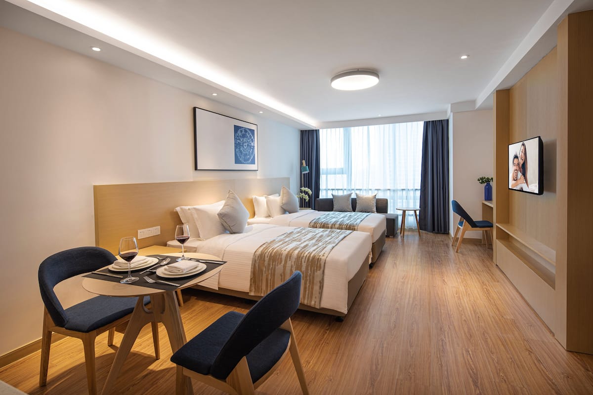 Une chambre d’hôtel moderne dotée d’un grand lit, d’une table à manger avec des chaises et offrant une vue sur la ville grâce à de grandes fenêtres.