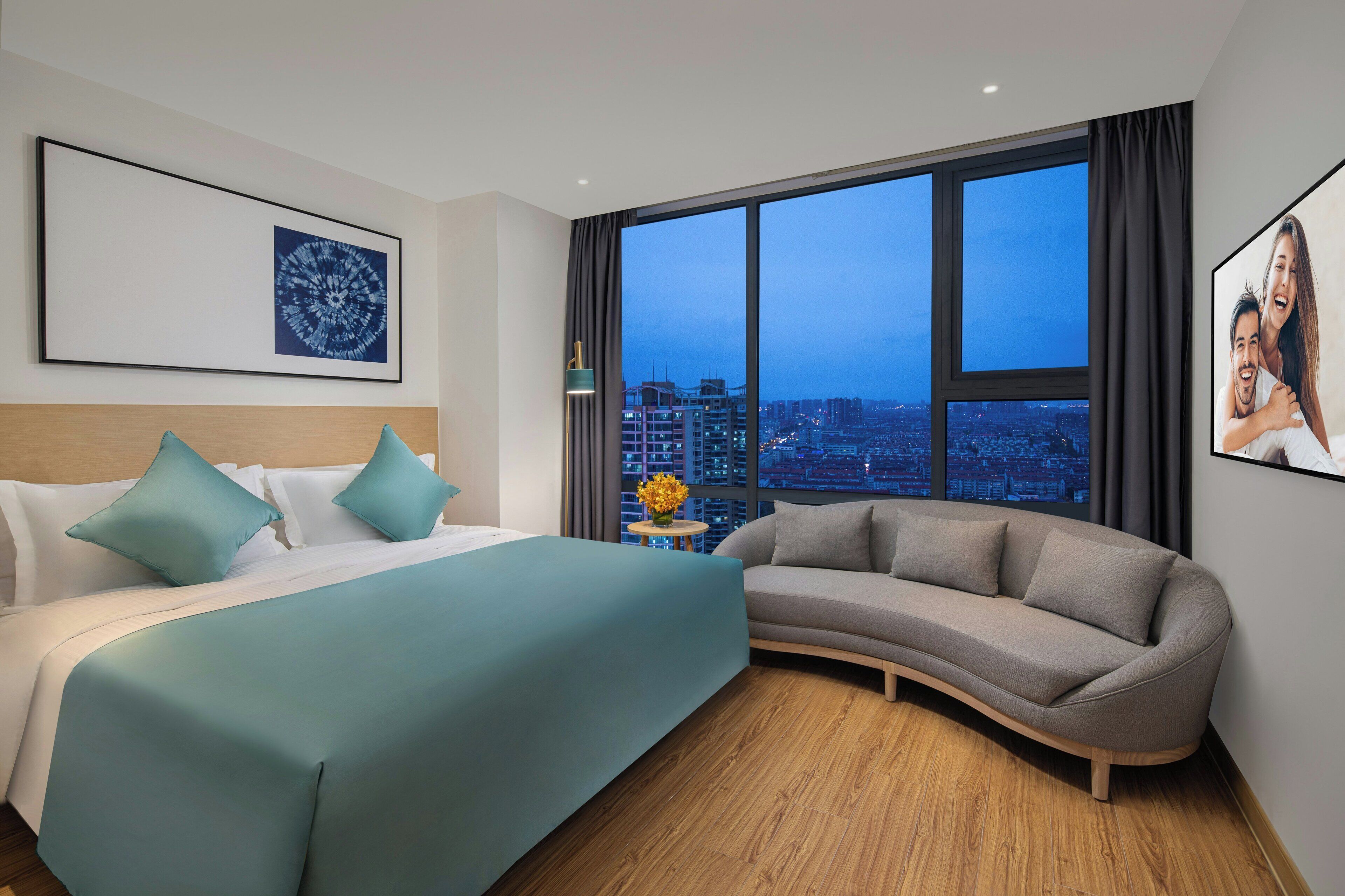 Una habitación de hotel con una cama, un sofá, un ventanal con vistas a la ciudad y un cuadro en la pared.