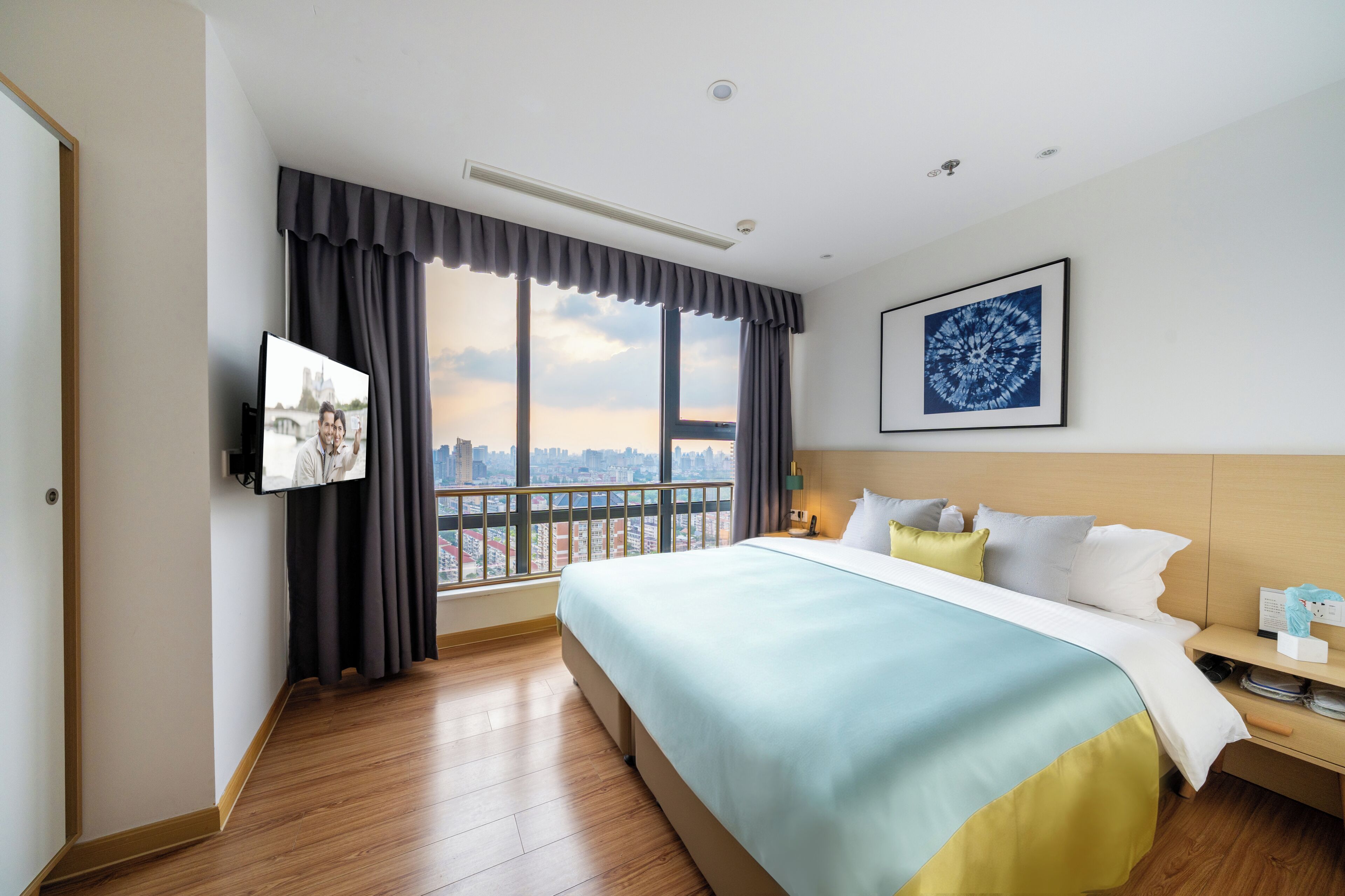 Una camera d'albergo con un letto grande, vista sulla città, una TV a schermo piatto e un quadro appeso al muro.