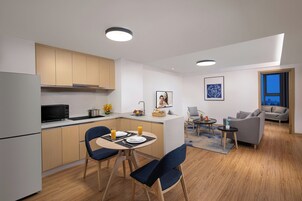 Una cocina moderna con comedor, una sala de estar con sofá y una mesa de centro, y vista de la ciudad a través de un ventanal.