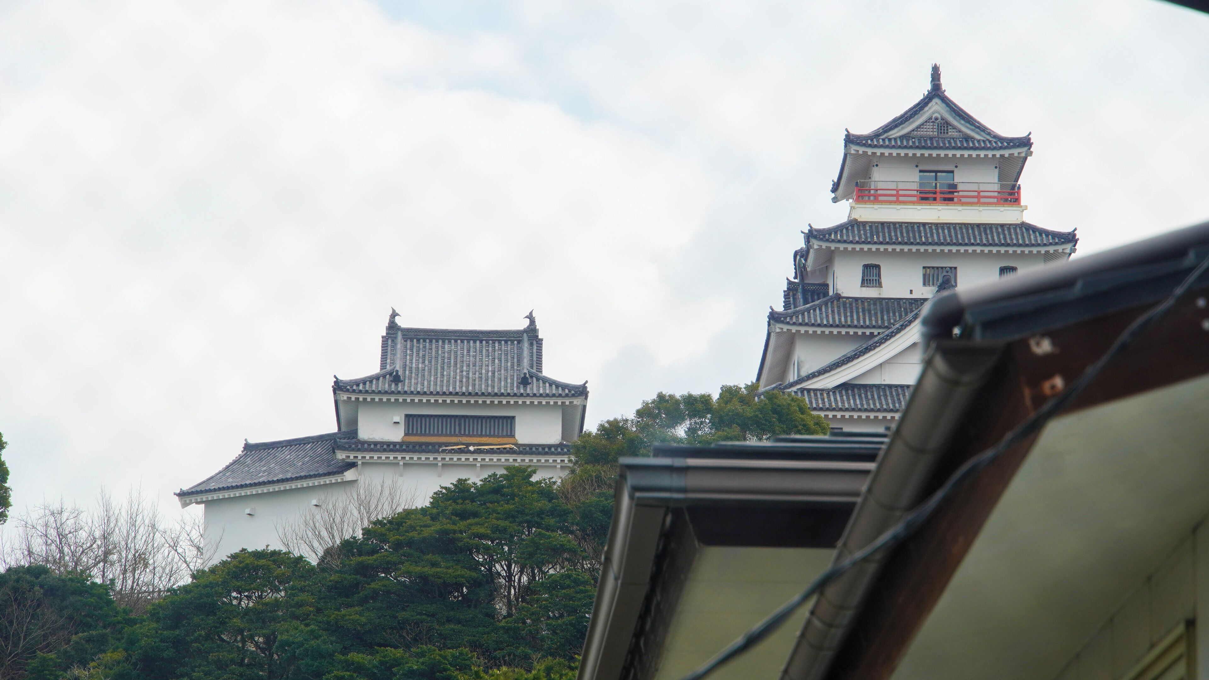A traditional Japanese castle with multiple tiers and a prominent red railing on the upper levels.