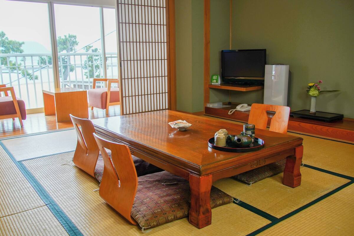 A traditional Japanese-style room with tatami flooring, a low table with a tea set, and a TV on a stand.