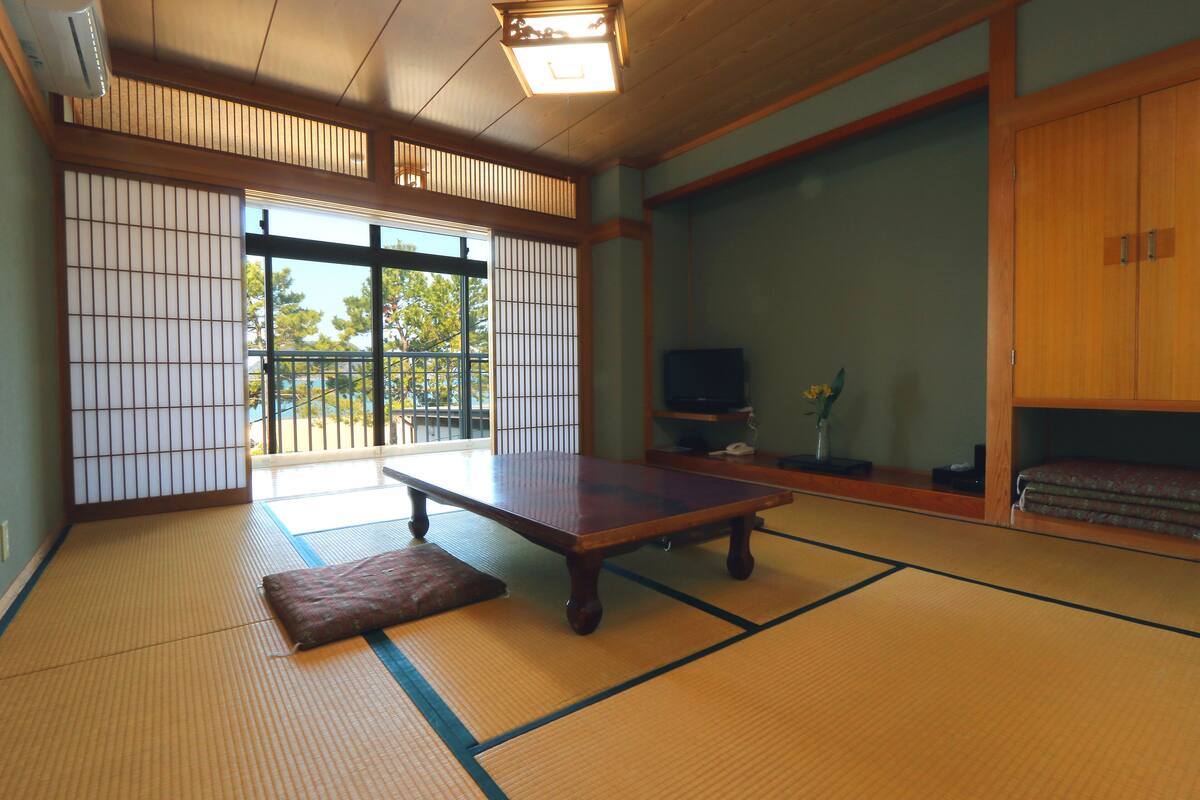 A traditional Japanese room with tatami flooring, a low wooden table, sliding doors, and a television.