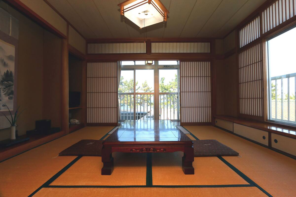 A tatami mat room with a low wooden table, sliding shoji doors, and a view through the doors.
